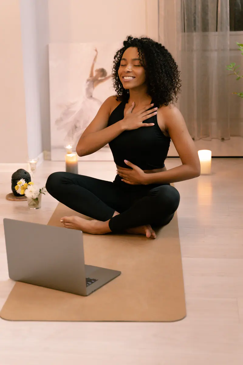 A person sitting cross-legged on a mat, one hand on her chest, following a guided breathing session by candlelight.